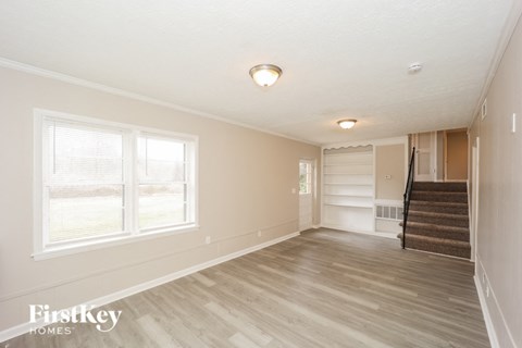 A spacious room with wooden flooring and a staircase leading to another room.