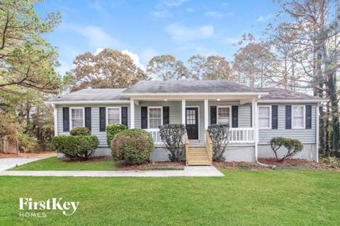 a white bungalow with black shutters and a lawn in front of it