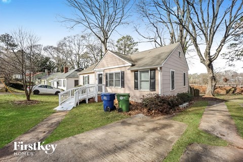 a small house with a white porch and a driveway with trash cans