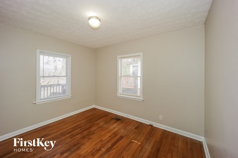 a bedroom with a hard wood floor and two windows