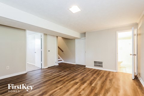 A spacious room with wooden floors and white walls, with a staircase leading to another level.