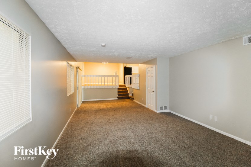 a spacious living room with a carpeted floor and a staircase