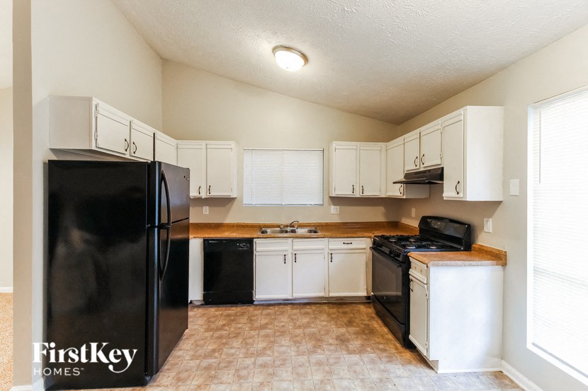 an empty kitchen with white cabinets and a black refrigerator