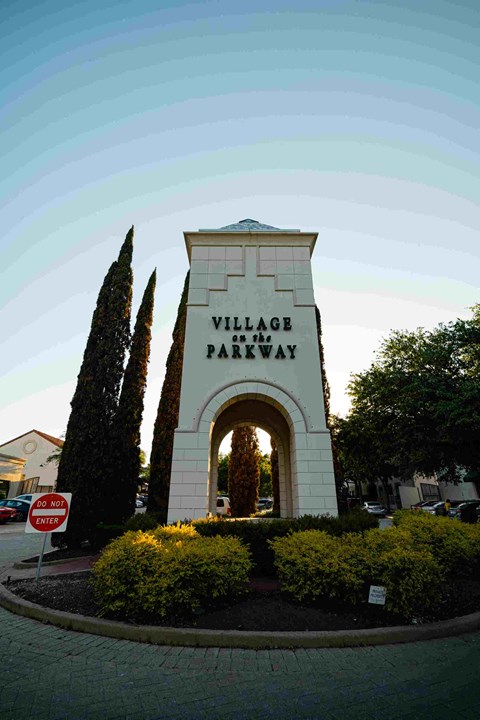 A sign that says "Village Parkway" is in front of some trees.