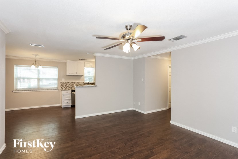 an empty living room with a ceiling fan and a kitchen