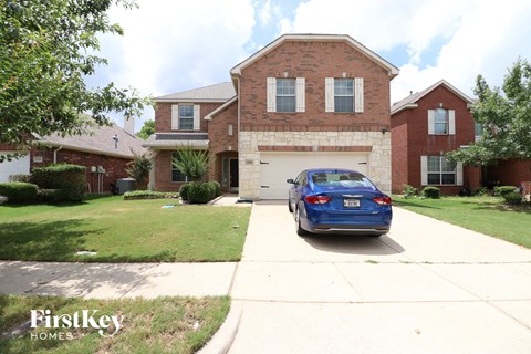A blue car is parked in front of a brick house.