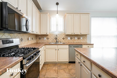 A kitchen with a black stove top oven and a black microwave above a black and white checkered backsplash.