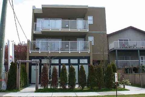 A modern two-story apartment building with balconies and a small garden in front.