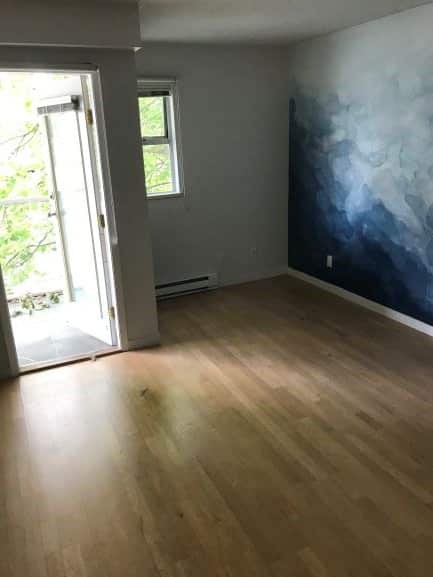 A room with a wooden floor and a wall with a blue and white painting.