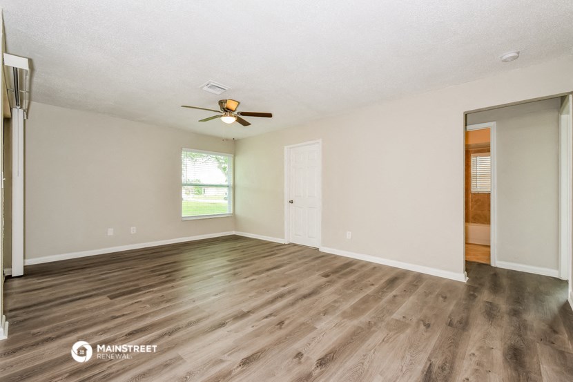 the spacious living room with hardwood flooring and a ceiling fan