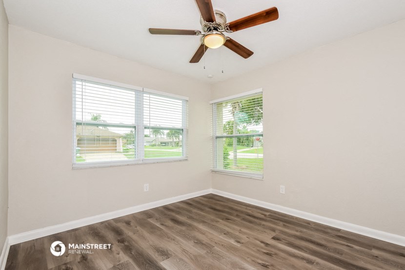 the spacious living room with two windows and a ceiling fan