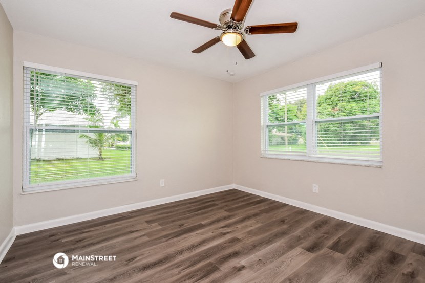 the spacious living room with two windows and a ceiling fan