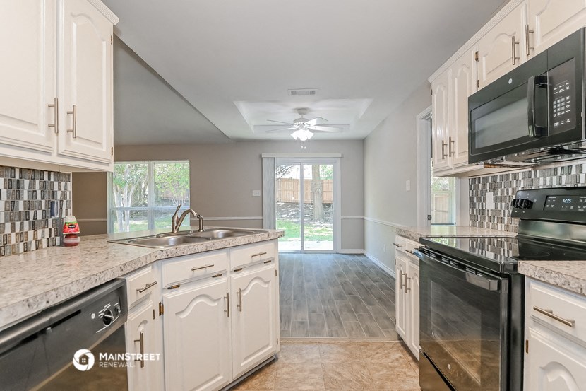 a kitchen with white cabinets and black appliances and a door to the yard