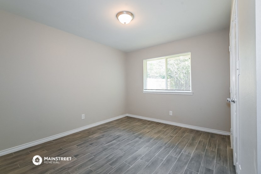 the bedroom of a rental house with wood flooring and a window