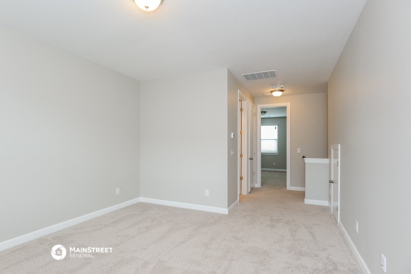 a spacious living room with white carpet and a hallway with a door to a bedroom