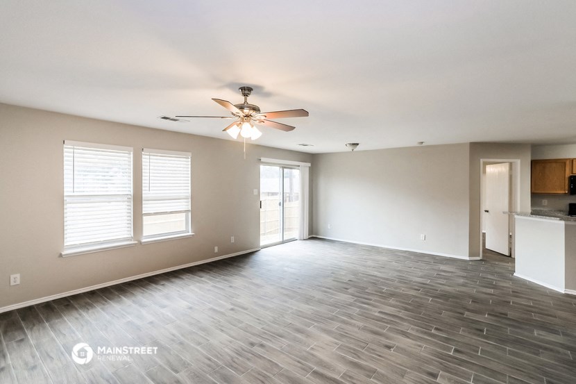 an empty living room with a ceiling fan and a kitchen