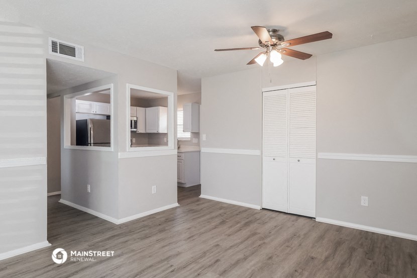 an empty living room with a ceiling fan and a kitchen