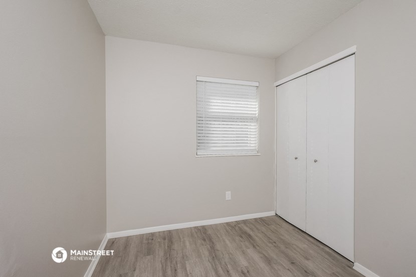 a bedroom with white walls and wood flooring and a closet
