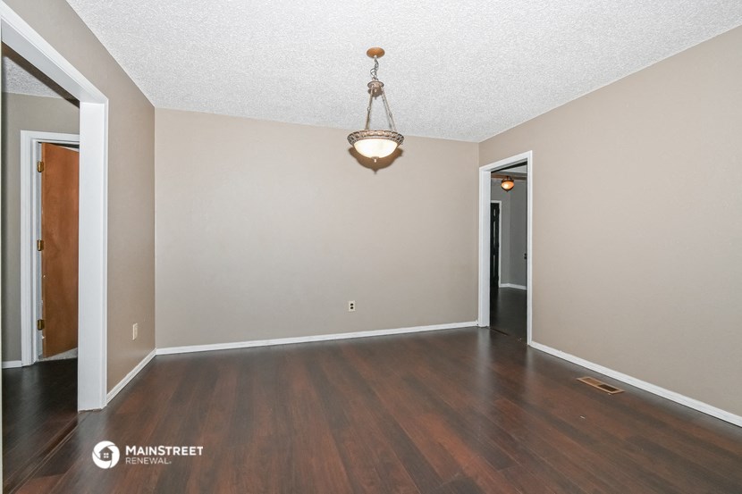an empty living room with wood flooring and a chandelier