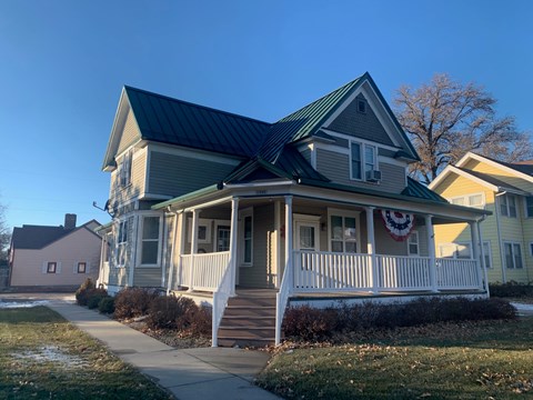 A house with a green roof and a porch with a flag on it.