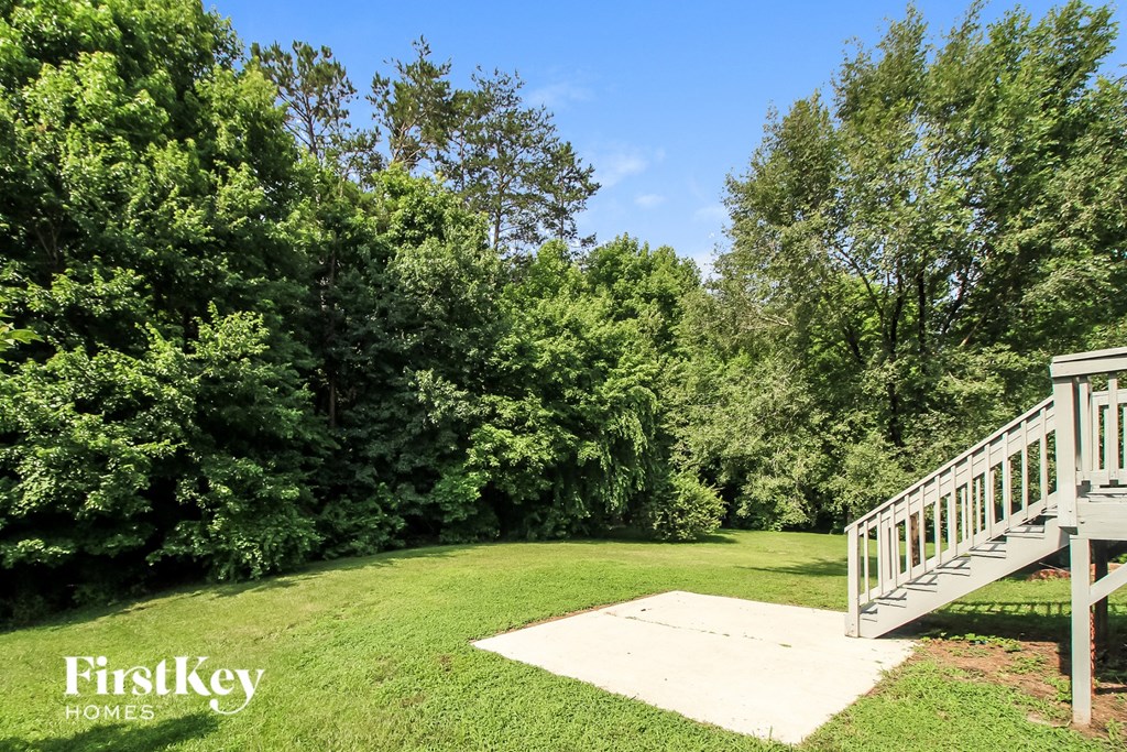a backyard with a wooden deck and a lawn and trees