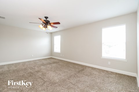 A spacious room with a ceiling fan and two windows.