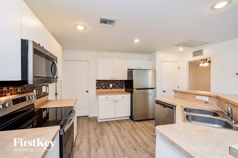 A kitchen with a stove top oven, microwave, refrigerator, and sink.