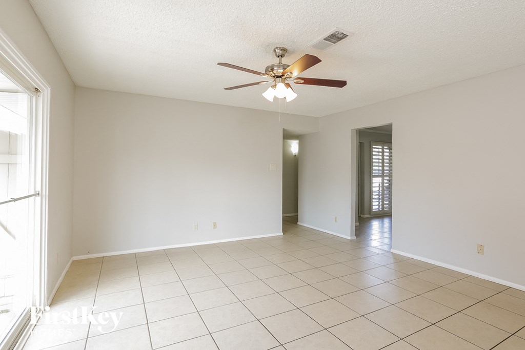 an empty living room with a ceiling fan and a tiled floor