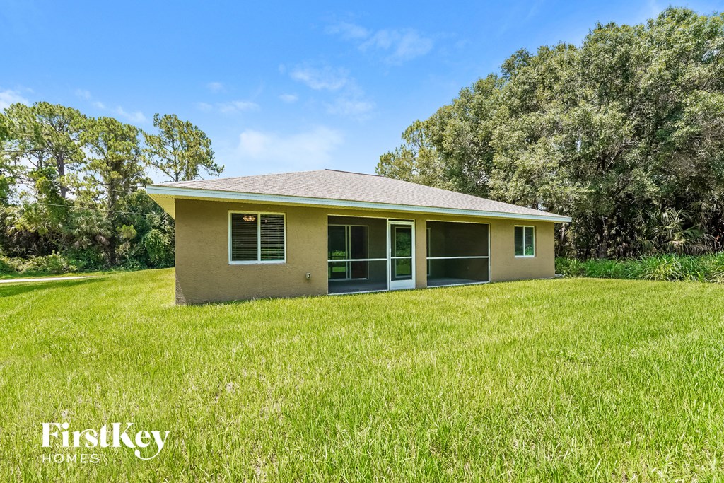 a small tan house in a grassy yard with trees