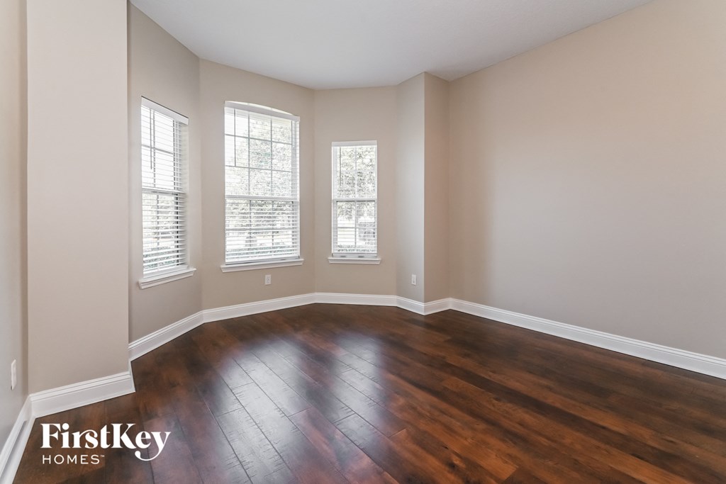 an empty living room with wooden floors and three windows