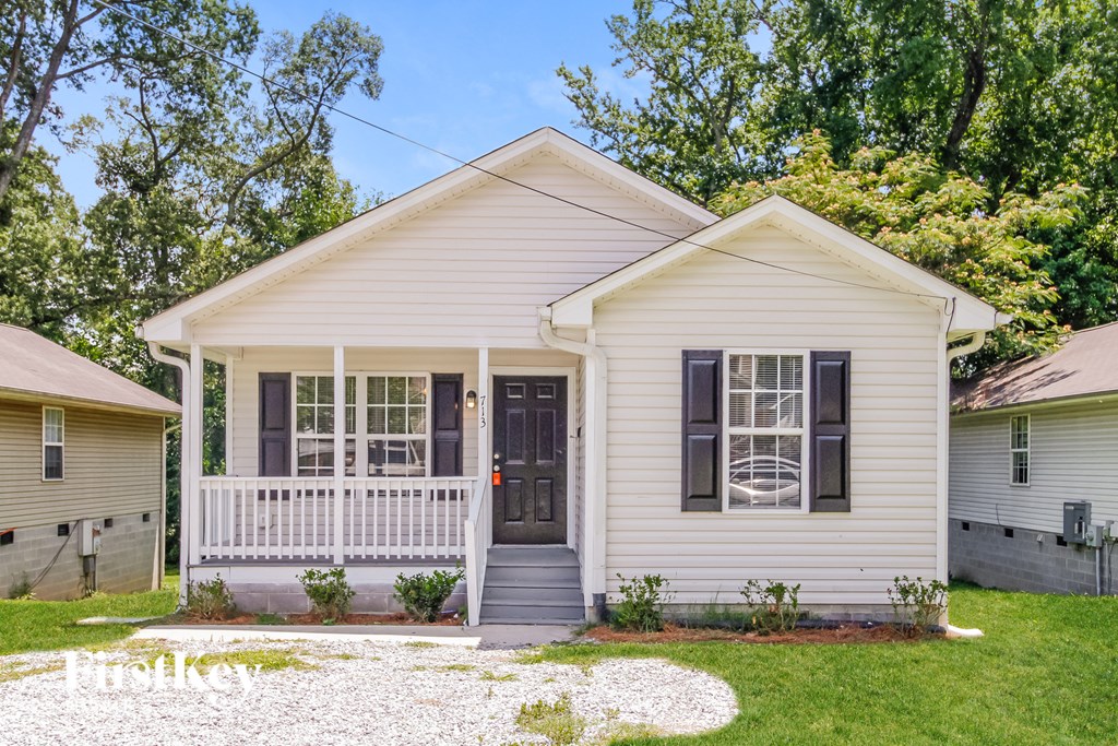 A white house with a black door and windows surrounded by greenery.