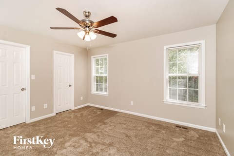 A spacious room with a ceiling fan and two windows.