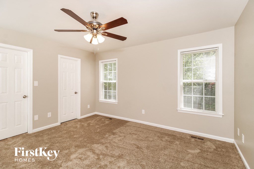 A spacious room with a ceiling fan and two windows.