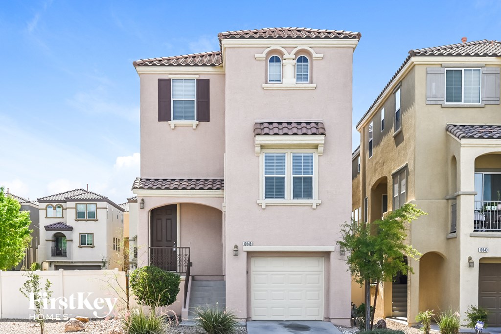 a beige house with two garage doors and a sidewalk
