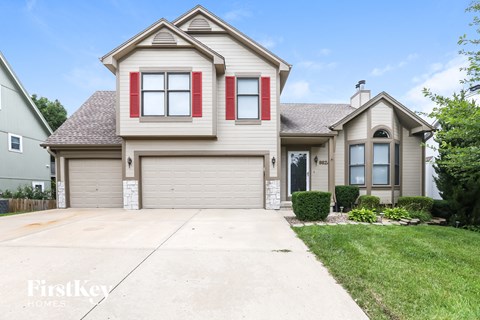 a beige house with red shutters and a driveway