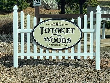 A sign that says "Totoken Woods" is in front of a white picket fence.