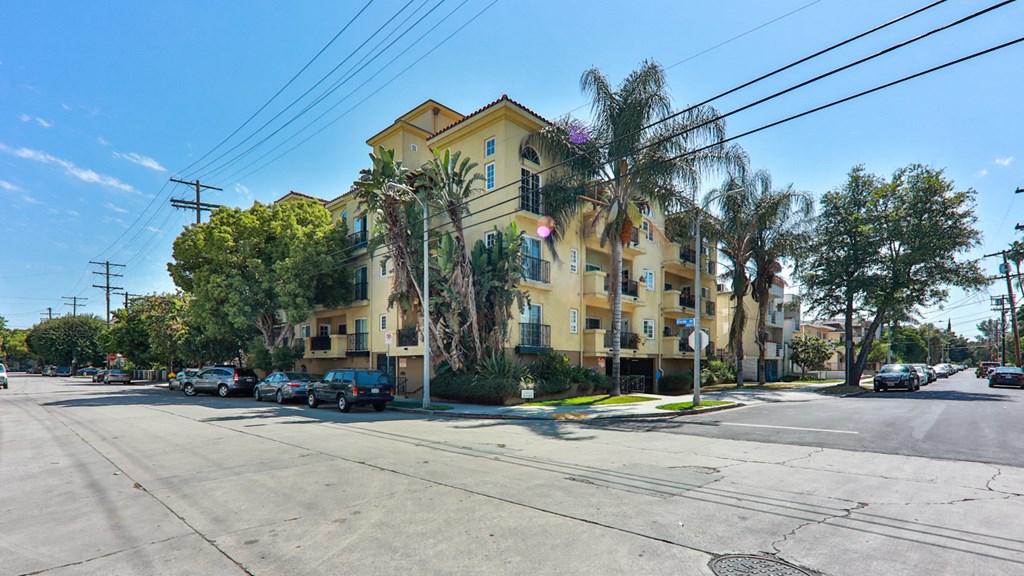 a yellow apartment building on a street corner with palm trees