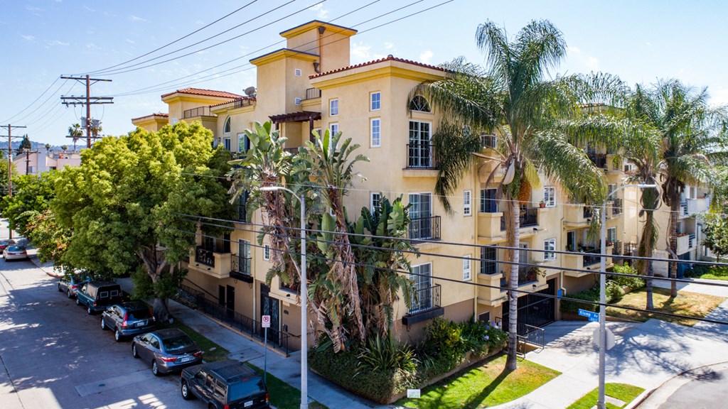 an apartment building with palm trees and cars parked in front of it
