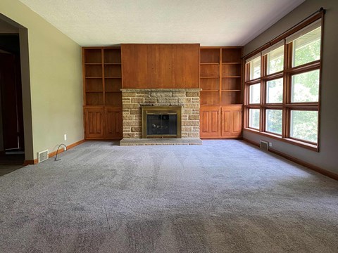 A living room with a fireplace and a grey carpet.