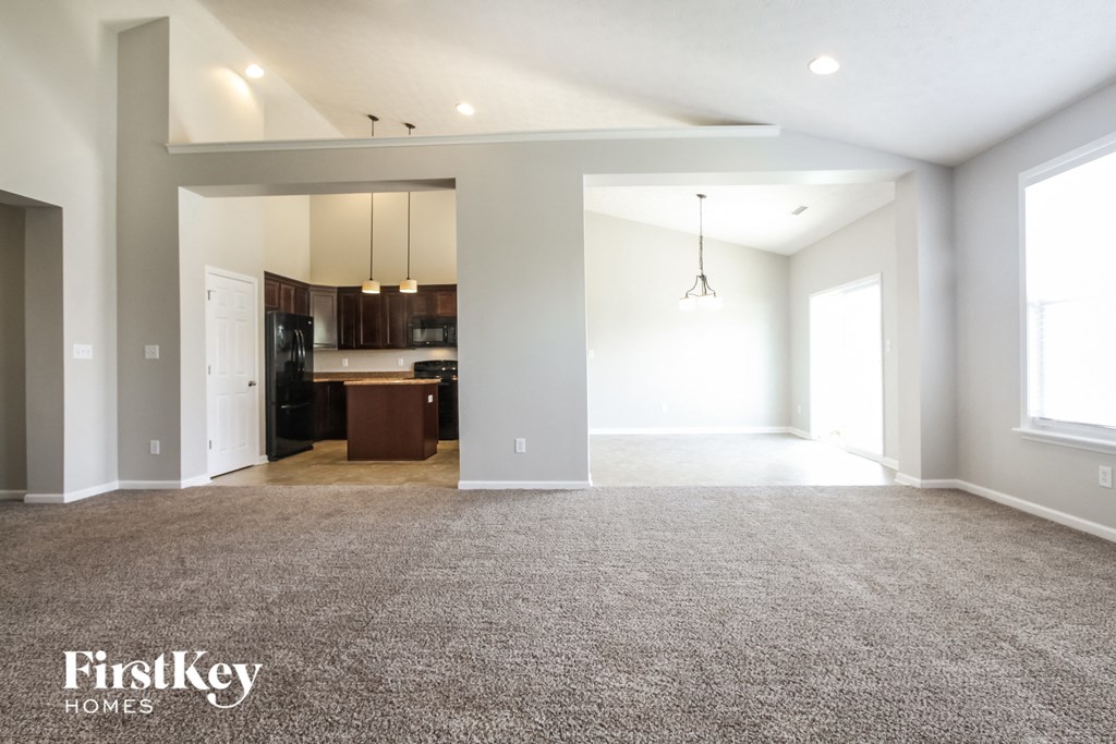an empty living room with carpet and a kitchen