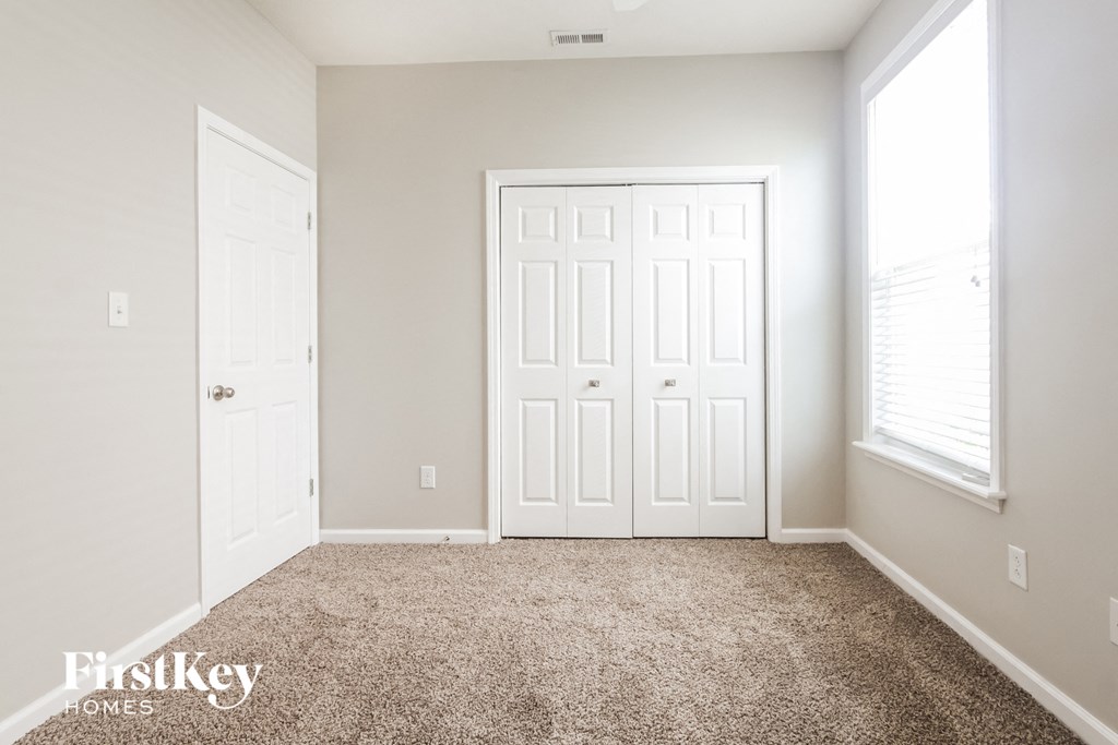a clean carpeted room with two doors and a window