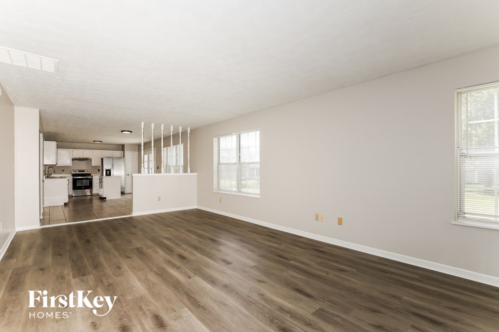 A spacious room with wooden flooring and a kitchen area in the background.