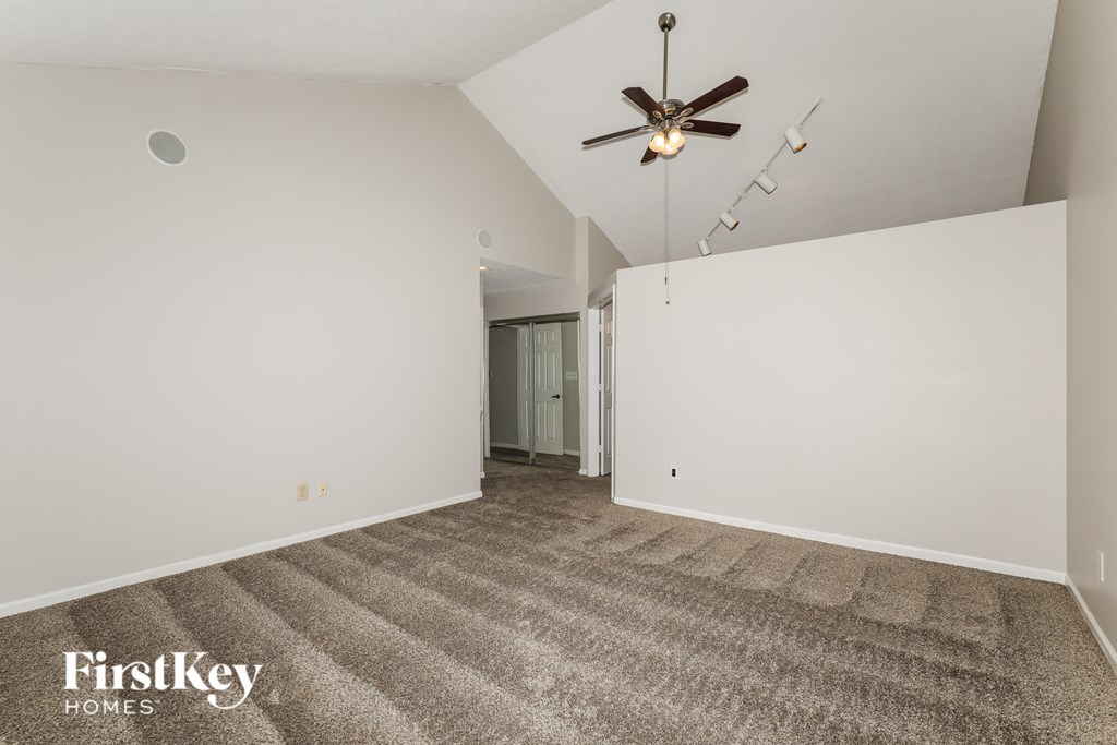 A carpeted room with a ceiling fan and a doorway leading to another room.