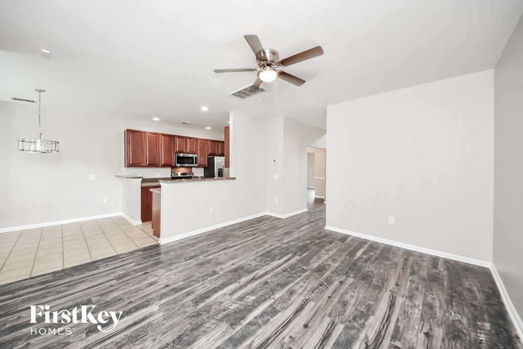 an empty living room with a ceiling fan and a kitchen