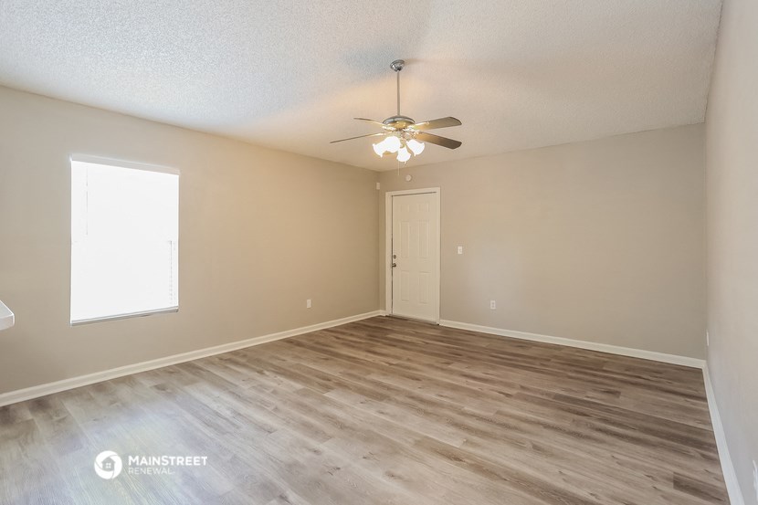 the spacious living room with wood flooring and a ceiling fan