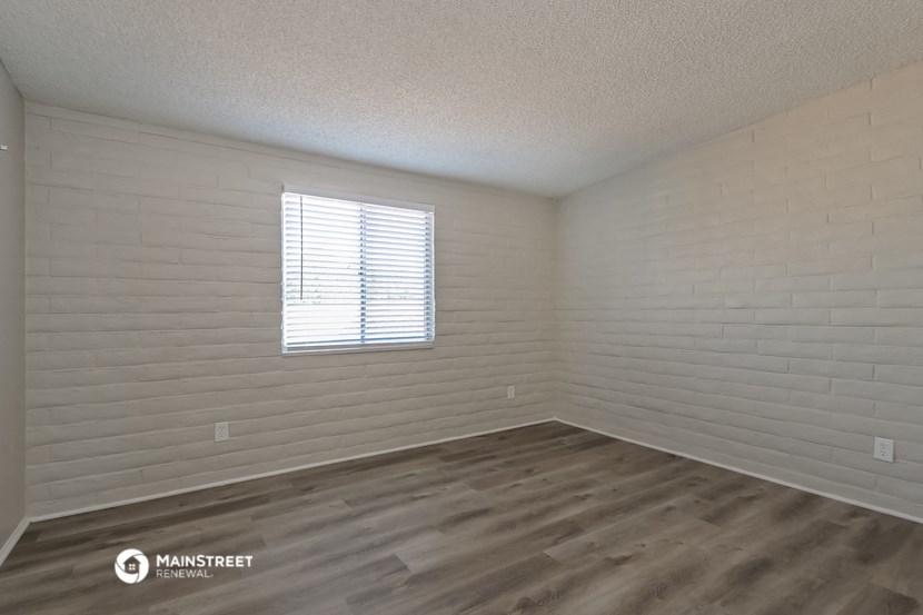 the spacious living room with wood flooring and white brick walls