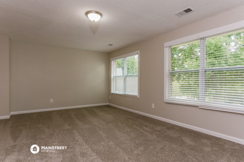 the spacious living room with two windows and carpeted flooring