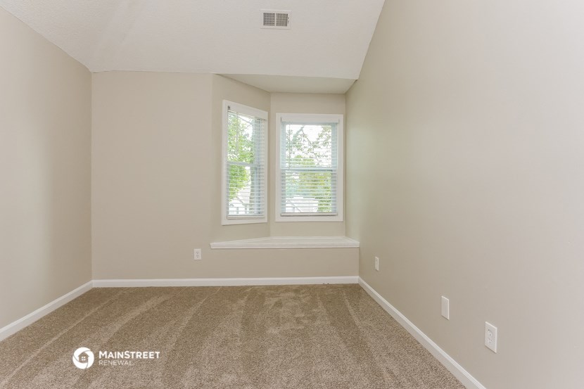 the spacious living room with two windows and carpeting