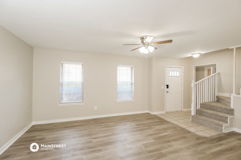 an empty living room with a staircase and a ceiling fan