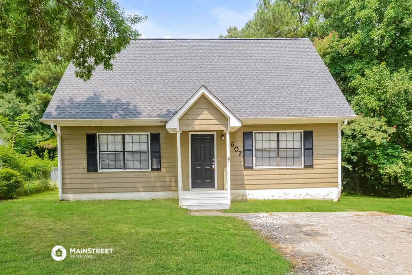 a small yellow house with a gray roof and a driveway